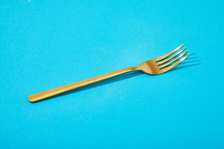 metal shiny golden fork on blue backgroundの写真素材