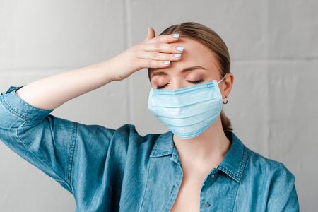 woman in medical mask touching forehead with closed eyesの写真素材