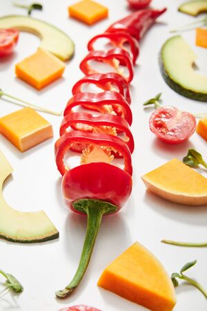 Selective focus of microgreens, cut chili pepper, pumpkin and cherry tomato with avocado slices on whiteの写真素材