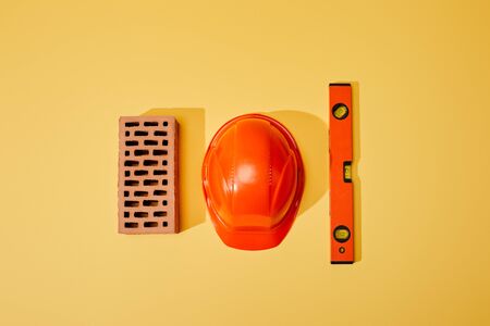 top view of brick, orange helmet and spirit level on yellow backgroundの写真素材