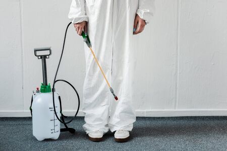 cropped view of person in white hazmat suit with disinfect in office, coronavirus conceptの写真素材