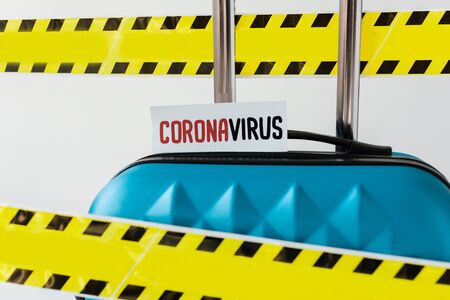 close up view of blue suitcase with coronavirus card in yellow and black hazard warning safety tape isolated on whiteの写真素材