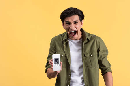 KYIV, UKRAINE - NOVEMBER 18, 2019: aggressive man yelling and showing smartphone with uber app on screen, isolated on yellowのeditorial素材