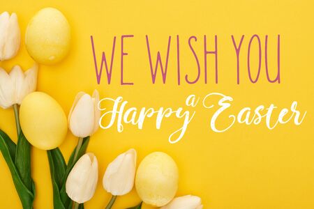 top view of tulips and painted Easter eggs on colorful yellow background with we wish you a happy...