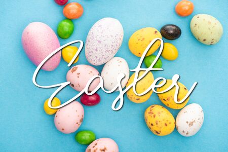 Top view of bright colorful sweets and easter eggs on blue background with Easter illustrationの写真素材