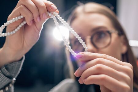 selective focus of attractive stylist looking at pearl necklace