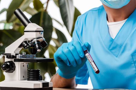 cropped view of scientist in latex glove holding test tube with sample and coronavirus lettering...