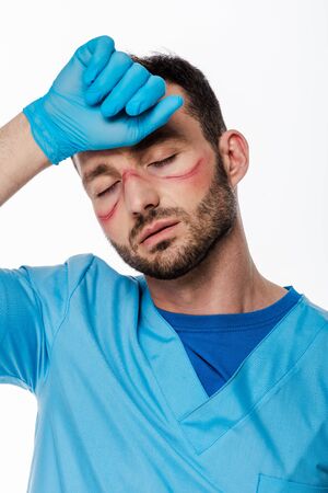 tired doctor with marks on face and closed eyes touching forehead isolated on white