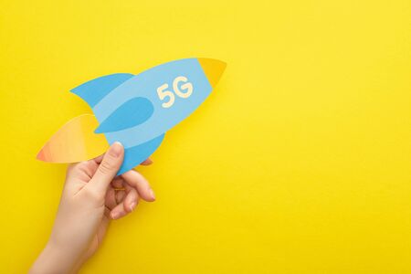 cropped view of woman holding paper rocket with 5g lettering on yellow background