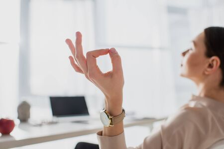 selective focus of businesswoman meditating with gyan mudra at workplaceの写真素材