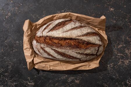 top view of organic brown bread loaf on paper on stone black surface