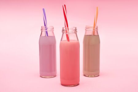 Bottles of colorful berry, strawberry and chocolate milkshakes with drinking straws on pinkの写真素材