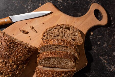 cut whole grain bread on cutting board near knife on stone black surface