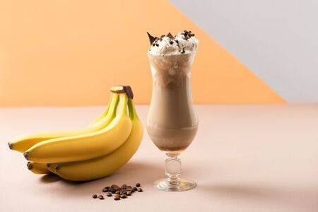 Glass of milkshake with chocolate morsels near bananas and coffee grains on beige, grey and orangeの写真素材
