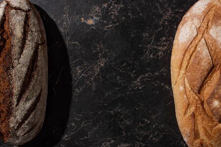 top view of fresh baked brown and white bread on stone black surface