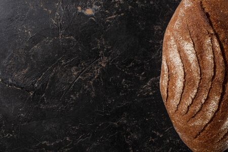 top view of fresh baked brown bread loaf on stone black surface