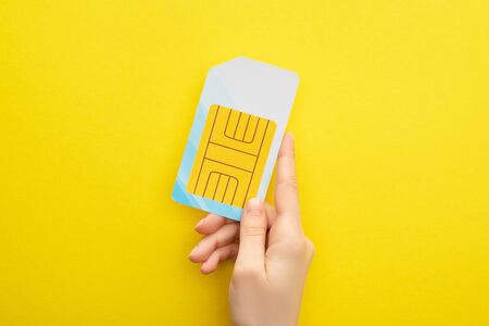 cropped view of woman holding sim card on yellow backgroundの写真素材