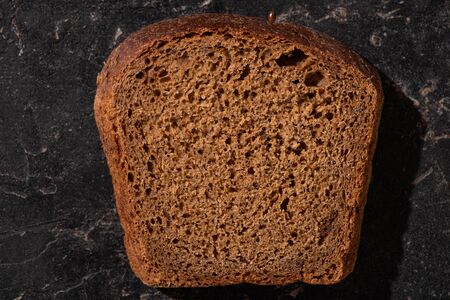 top view of fresh baked brown bread slice on stone black surface