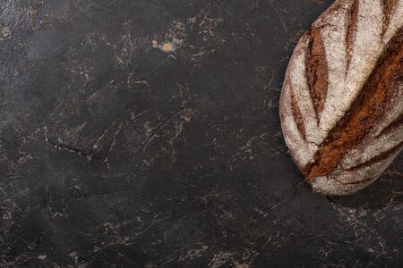 top view of organic brown bread loaf on stone black surface
