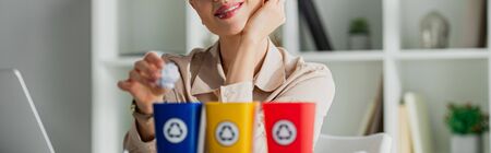 panoramic shot of smiling businesswoman throwing crumpled paper into recycling buckets