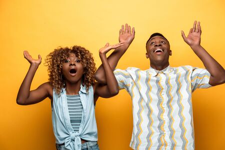 shocked african american couple with open mouths gesturing on yellow colorful background