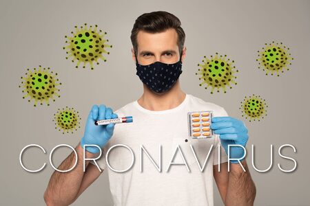 Man in safety mask holding blister with pills and test tube with blood sample isolated on grey, bacteria and coronavirus illustrationの写真素材