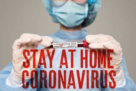 Selective focus of doctor holding test tube with blood sample of coronavirus lettering isolated on grey, stay at home coronavirus illustrationの写真素材