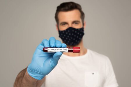 Selective focus of man in latex glove holding test tube with blood sample and coronavirus lettering...