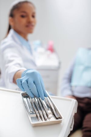 selective focus of african american dentist in latex glove taking dental instrumentの写真素材