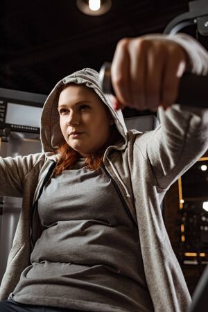 selective focus of concentrated overweight girl doing arms extension exercise on fitness machine