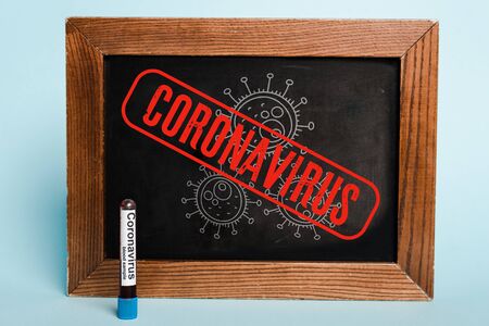 coronavirus lettering written on chalkboard near test tube with blood sample on blue backgroundの写真素材