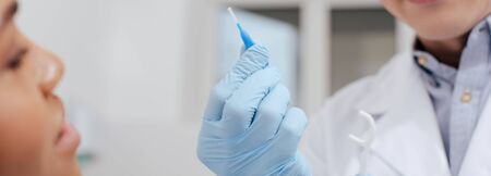 panoramic shot of dentist holding floss stick and inter dental cleaning brush near african american womanの写真素材