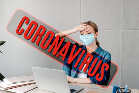 woman in medical mask touching forehead while working with laptop in office, coronavirus illustrationの写真素材