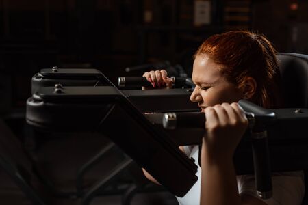 purposeful overweight girl doing arms extension exercise on fitness machine