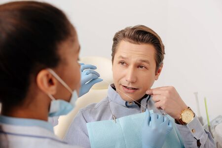 selective focus of african american dentist in latex gloves holding dental floss near patient pointing with finger at faceの写真素材