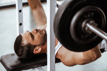 selective focus of handsome man exercising with barbell in gymの写真素材