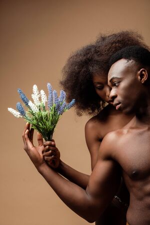 sexy naked african american couple posing with plant on beigeの写真素材