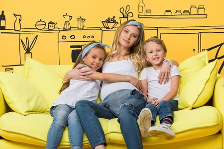 happy pregnant mother hugging with kids on sofa isolated on yellow, interior illustrationの写真素材