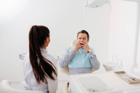 back view of african american dentist sitting near scared patient touching faceの写真素材