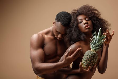 sexy naked african american couple posing with pineapple on beigeの写真素材