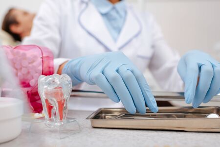 cropped view of dentist in latex gloves touching stainless dental instruments