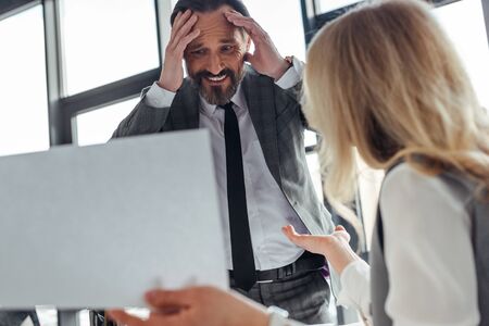 Selective focus of smiling businessman near businesswoman holding paper in officeの写真素材