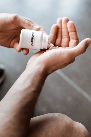 cropped view of sportive man holding bottle with probiotic lettering and pills