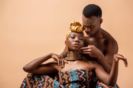 sexy naked tribal afro woman covered in blanket posing near man isolated on beigeの写真素材