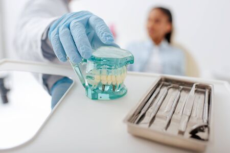 selective focus of dentist in latex glove taking teeth model near dental instruments