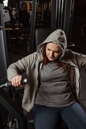purposeful overweight girl doing arms extension exercise on fitness machine