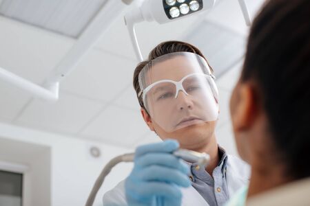 low angle view of dentist in face shield and latex gloves holding dental instrument near african american womanの写真素材