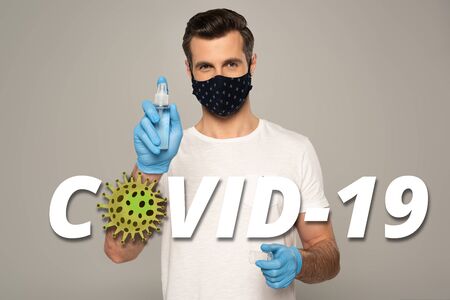 Man in latex gloves and safety mask holding hand sanitizer isolated on grey, covid-19 illustrationの写真素材