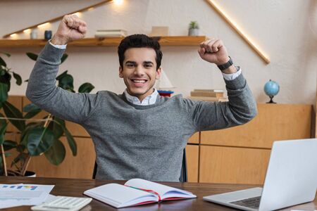 Excited businessman looking at camera and smiling at table in officeの写真素材