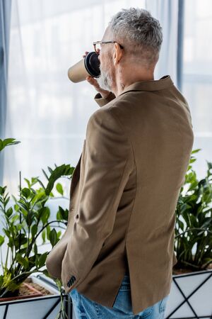 back view of businessman drinking coffee to go near plantsの写真素材